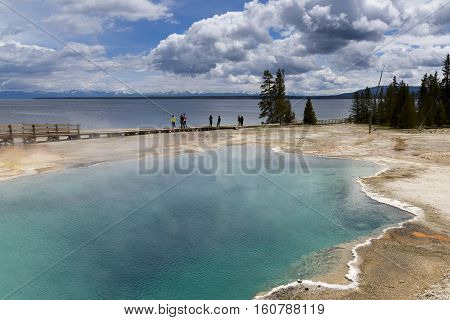 Yellowstone United States - May 31 2015: Clear aqua hot spring with deep central hole steam and limy shoreline people on boardwalk West Thumb area of Yellowstone National Park Wyoming.