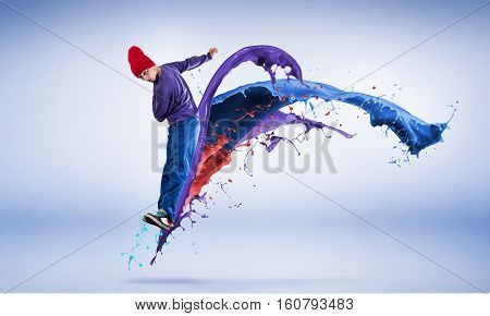 Young male dancer in jump on white background with colorful paint plashes