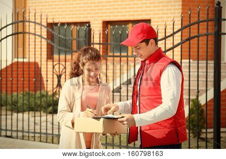 Young woman signing receipt for delivering parcel from male courier