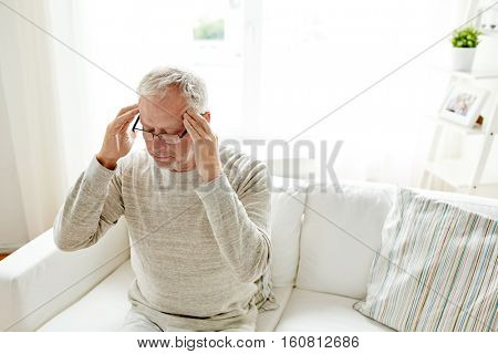 healthcare, pain, stress, age and people concept - senior man suffering from headache at home