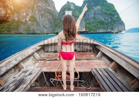 Sexy girl wearing a red bikini in a happy mood on long boat. Lady on boat raises hand. Phi Phi island.