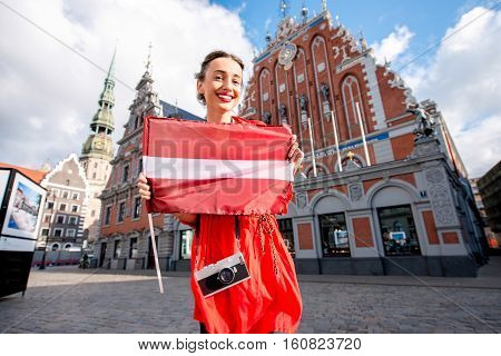 Portrait of a young female tourist with latvian flag on the main old town square in Riga. Woman having great vacations in Latvia