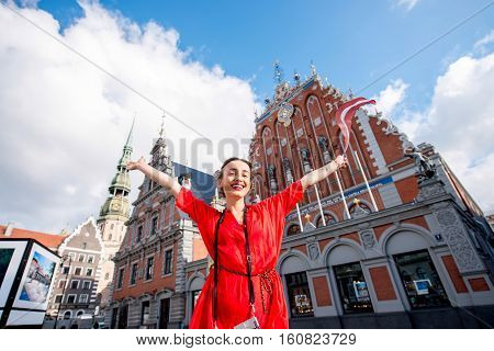 Portrait of a young female tourist with latvian flag on the main old town square in Riga. Woman having great vacations in Latvia
