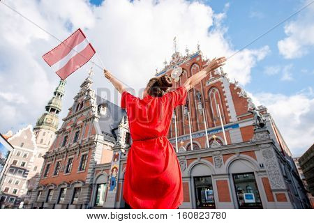 Young female tourist with latvian flag on the main old town square in Riga. Woman having great vacations in Latvia