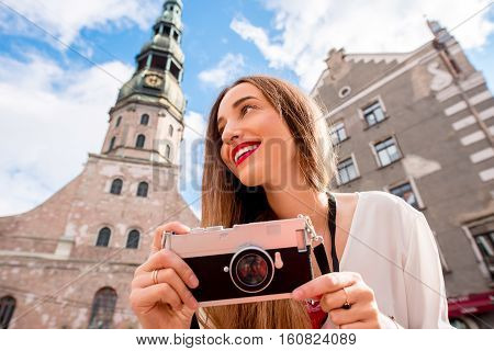 Portrait of a young female tourist with photo camera in front of saint Peter church in Riga. Woman having great vacations in Latvia