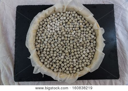 Flan or quiche dish with pastry and filled with ceramic baking beans on baking tray ready for oven.