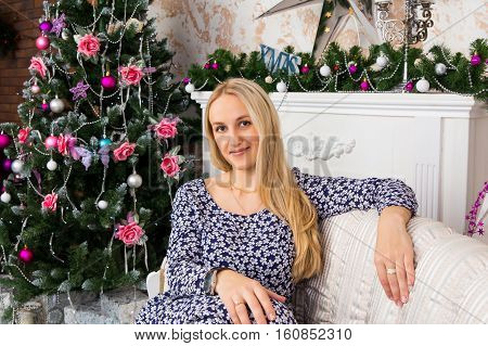 Beautiful lady sitting on sofa in room decorated for Christmas holidays