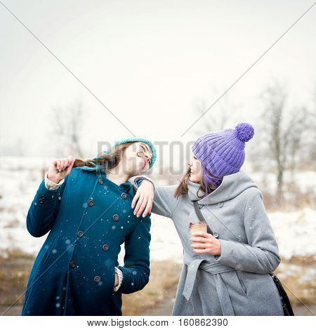 Two teenage girls having fun outdoors on snowy winter day in park. Two female friends enjoying outside in wintertime and laughing.