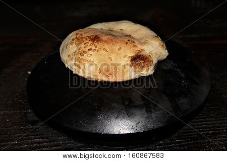 A small round loaf of pita bread baking on the saj.