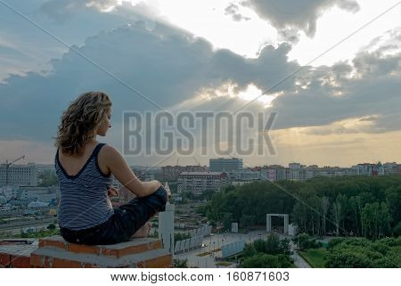 Young attractive woman relaxes on edge of high building roof