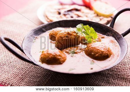 Freshly cooked spicy potato curry in frying pan or Hot and spicy Dum aloo served with tandoori roti or naan or indian bread or chapati and green salad, selective focus