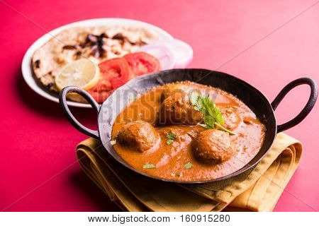 Freshly cooked spicy potato curry in frying pan or Hot and spicy Dum aloo served with tandoori roti or naan or indian bread or chapati and green salad, selective focus