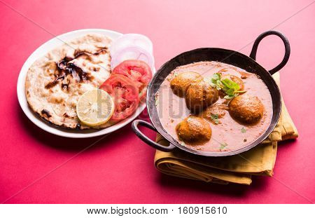 Freshly cooked spicy potato curry in frying pan or Hot and spicy Dum aloo served with tandoori roti or naan or indian bread or chapati and green salad, selective focus