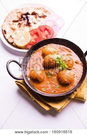 Freshly cooked spicy potato curry in frying pan or Hot and spicy Dum aloo served with tandoori roti or naan or indian bread or chapati and green salad, selective focus
