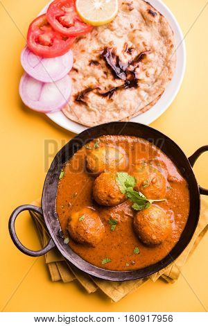 Freshly cooked spicy potato curry in frying pan or Hot and spicy Dum aloo served with tandoori roti or naan or indian bread or chapati and green salad, selective focus
