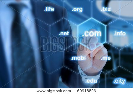 Businessman in blue touching the domain ending com on a hexagon grid in front of office background