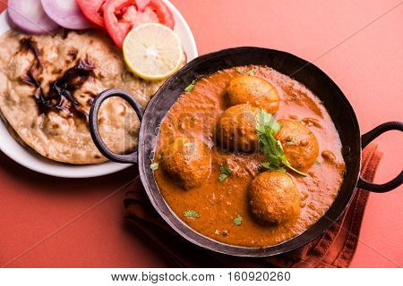 Freshly cooked spicy potato curry in frying pan or Hot and spicy Dum aloo served with tandoori roti or naan or indian bread or chapati and green salad, selective focus