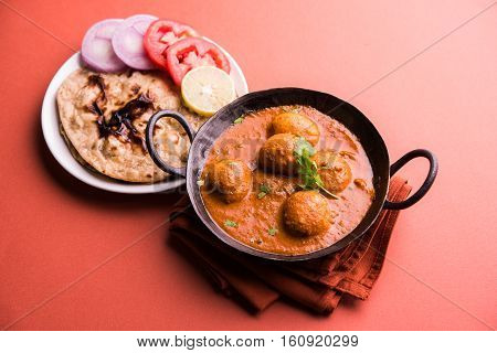 Freshly cooked spicy potato curry in frying pan or Hot and spicy Dum aloo served with tandoori roti or naan or indian bread or chapati and green salad, selective focus