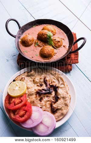 Freshly cooked spicy potato curry in frying pan or Hot and spicy Dum aloo served with tandoori roti or naan or indian bread or chapati and green salad, selective focus