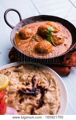 Freshly cooked spicy potato curry in frying pan or Hot and spicy Dum aloo served with tandoori roti or naan or indian bread or chapati and green salad, selective focus