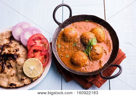 Freshly cooked spicy potato curry in frying pan or Hot and spicy Dum aloo served with tandoori roti or naan or indian bread or chapati and green salad, selective focus