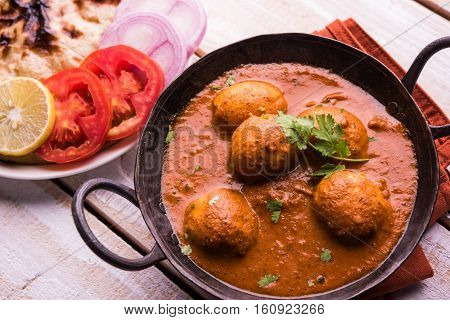Freshly cooked spicy potato curry in frying pan or Hot and spicy Dum aloo served with tandoori roti or naan or indian bread or chapati and green salad, selective focus