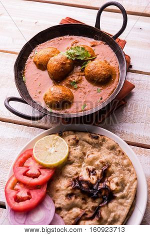 Freshly cooked spicy potato curry in frying pan or Hot and spicy Dum aloo served with tandoori roti or naan or indian bread or chapati and green salad, selective focus