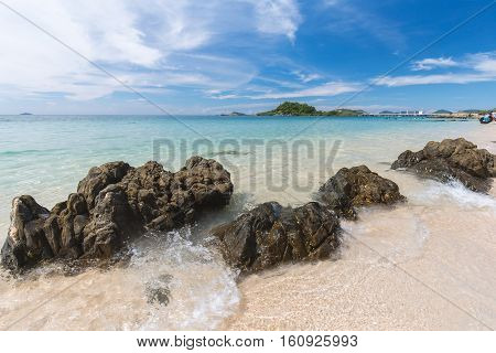 Clear water beach of blue sea with black rock and moving wave on sunny day in Thailand. Cloudy blue sky as background.
