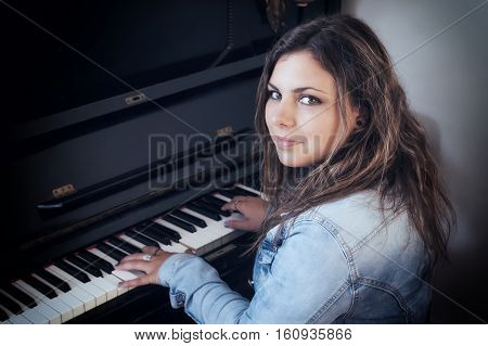Portrait of cool teenage girl playing the piano. The girl is looking at the camera. Photo is edited as a vintage with dark edges. All potential trademarks are removed.