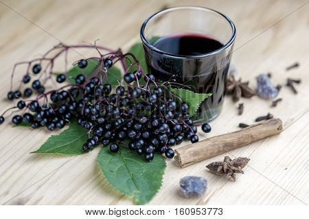 Glass of fresh elderberry syrup with cinnamon stick brown sugar star anise and elderberries on a wooden kitchen counter