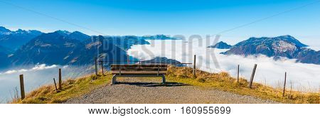 Aerial view. Peak. Bench to rest on the edge. Below clouds and a lake.