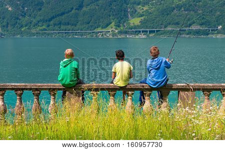 Fluelen, switzerland - Mai 31,2015. Three boys siting on the lake and fishing. Vacation by the lake