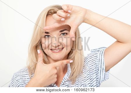 Gesturing finger frame. Beautiful young blond hair woman looking at camera and gesturing finger frame while standing against white background