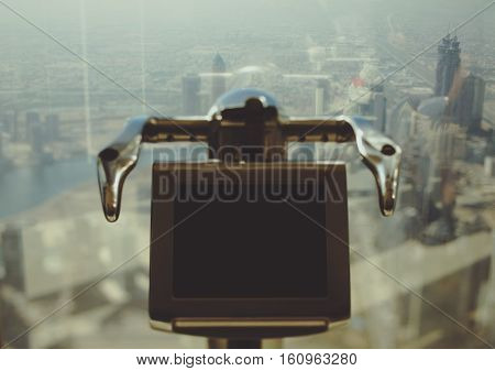 Tilt shift shooting of electronic telescope in front of window of Dubai skyscraper with top view of cityscape on summer day