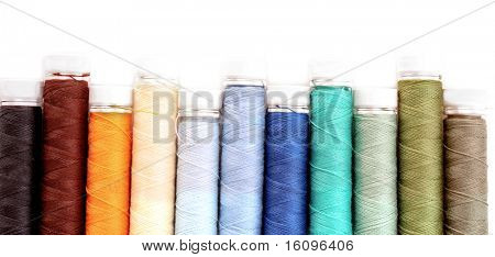 Pile of coloured bobbins of lurex thread isolated on white
