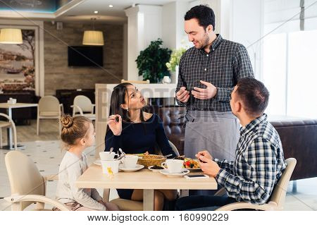 Friendly smiling waiter taking order at table of family having dinner together.