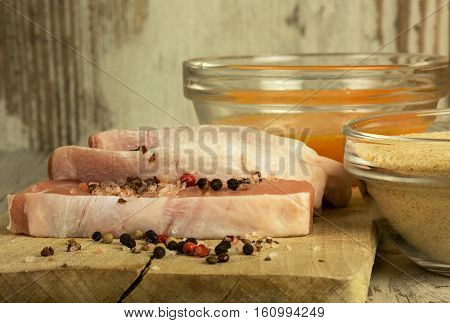 Three pieces of fresh raw pork chops bowls with bread crumbs and eggs to the breading meat peppercorns and salt crystals. Selective focus.Close horizontal side view.