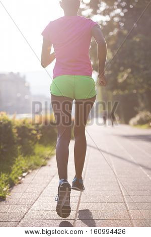 Beautiful young sporty african american woman running at early morning jogging with city sunrise scene in background