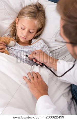 Confident Pediatrician Litening Childs Breath With Stethoscope While She Lying In Bed