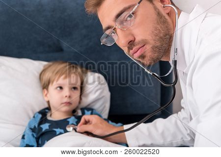 Pediatrician Litening Childs Breath With Stethoscope And Looking At Camera While He Lying In Bed
