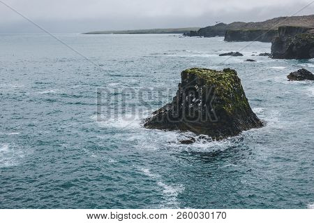 Scenic Shot Of Rocks And Cliff In Blue Ocean In Arnarstapi, Iceland On Stormy Day