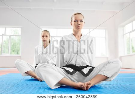 Two Young Karate Girl Sittting In Lotus Position After Training In Light Gym. Sporty Women Wearing I