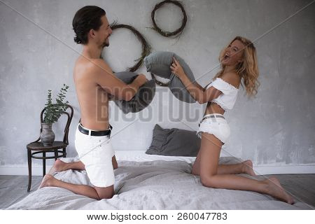 Young Beautiful Couple In White Fighting With Pillows On Modern Bed In Loft Design Bedroom ,having F