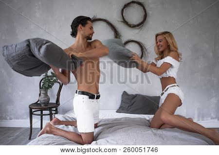 Young Beautiful Couple In White Fighting With Pillows On Modern Bed In Loft Design Bedroom ,having F
