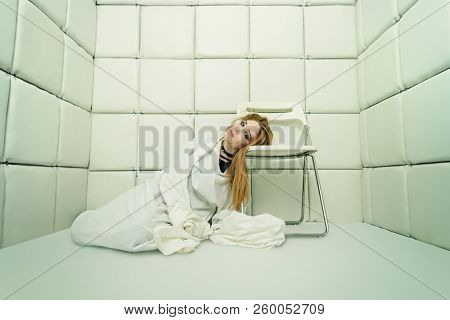 Portrait of a crazy girl dressed in a straitjacket in an isolated room in a madhouse.