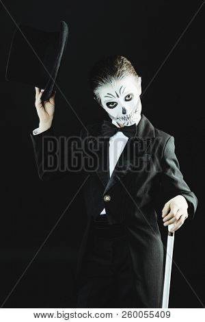 Portrait of a child boy with carnival make-up of a skeleton wearing elegant tail-coat. Studio shot over black background. Halloween. Dia de los muertos. The Day of the Dead.