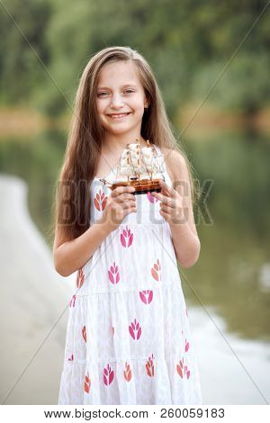 girl playing with a toy sailing ship by the river