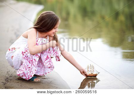 girl playing with a toy sailing ship by the river