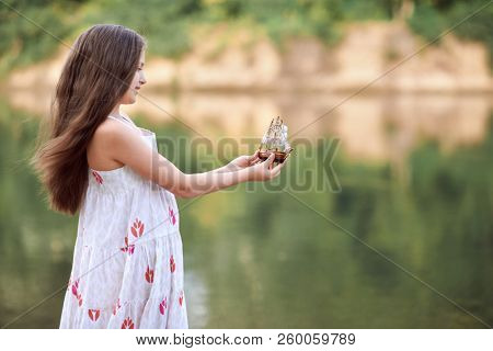 girl playing with a toy sailing ship by the river