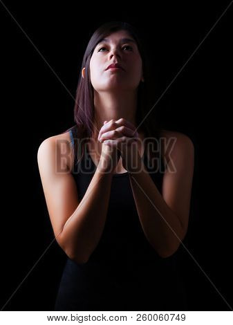 Faithful woman praying, hands folded in worship to god with looking up in religious fervor, on a black background. Concept for religion, faith, prayer and spirituality.